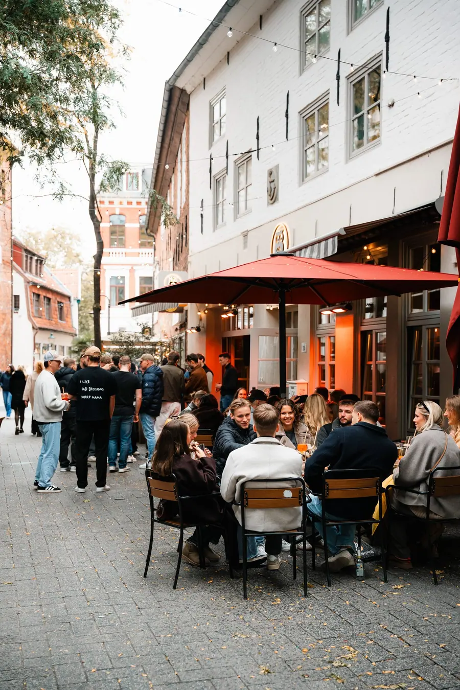 Volle Tische unter einem roten Sonnenschirm auf der Straße vor der Eule