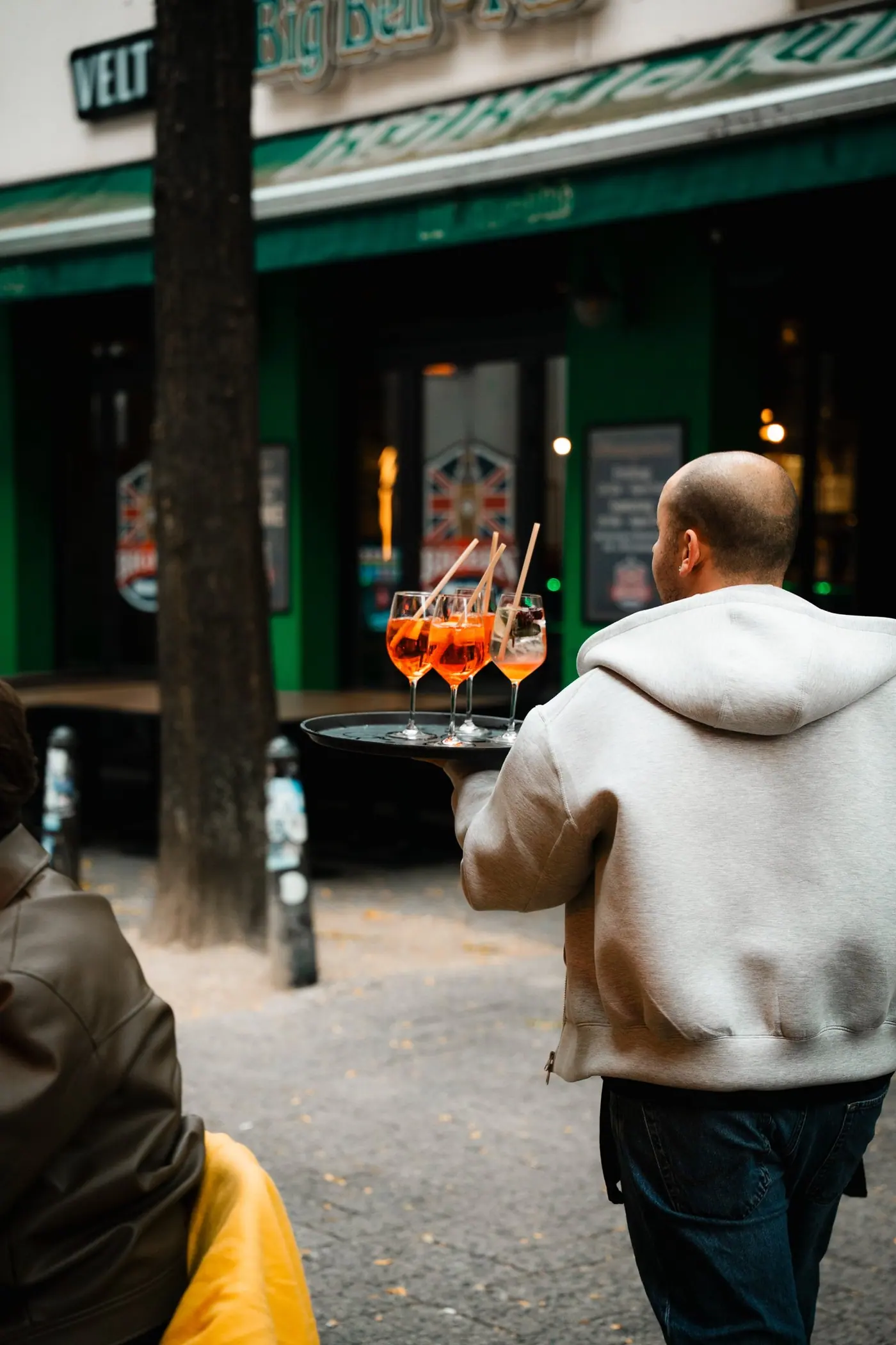 Ein Mitarbeiter trägt ein Tablett mit drei Aperol Spritz über die Straße