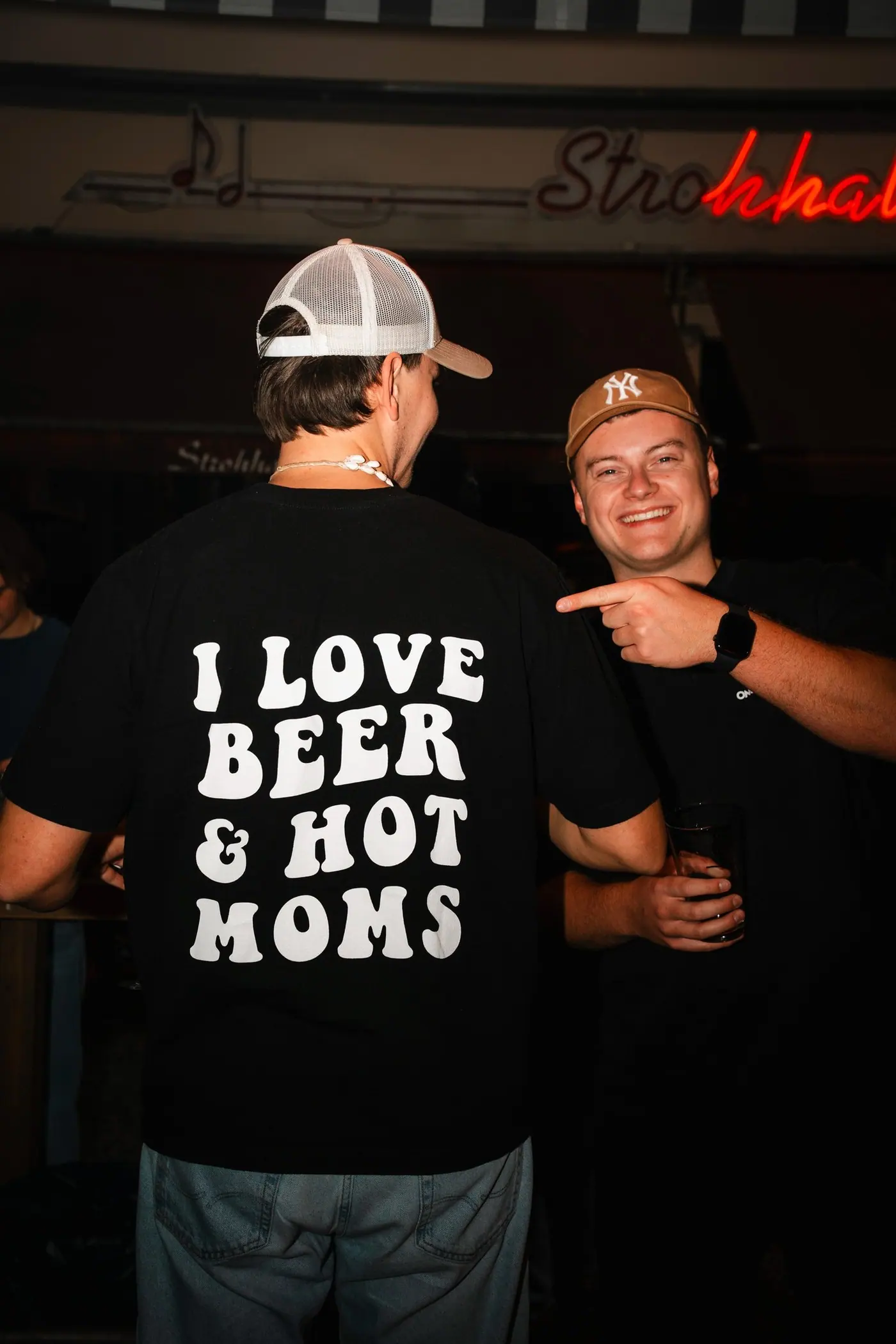 Zwei Gäste lachen, einer zeigt den Aufdruck auf seinem T-Shirt