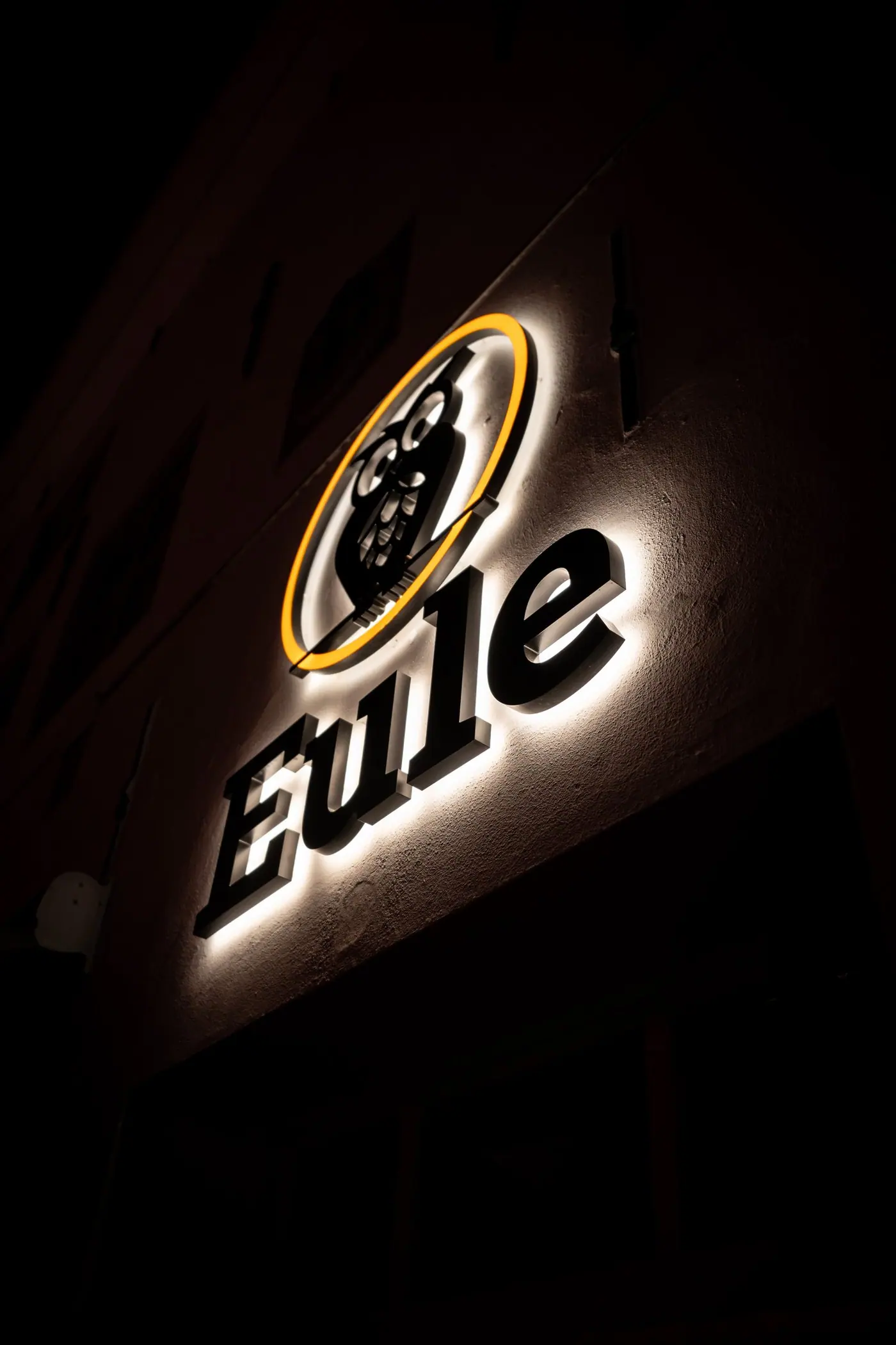 Das beleuchtete Eule-Schild mit dem Eulenlogo bei Nacht