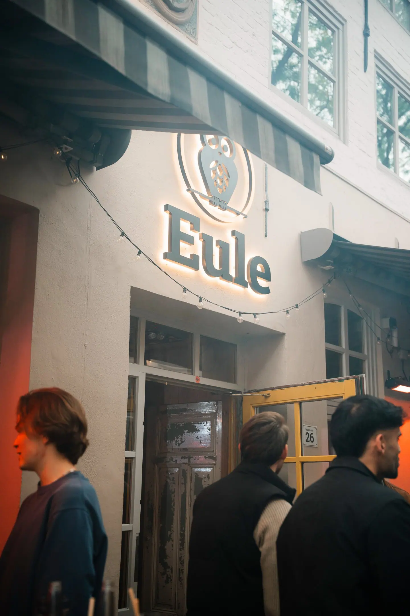 Der beleuchtete Eule-Schriftzug mit Eulenlogo über dem Eingang Wallstraße 26